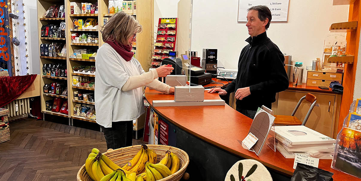 Im Weltladen Mannheim: Ein Kundin steht am Tresen und kauft Produkte, dahinter steht ein Mitarbeiter.